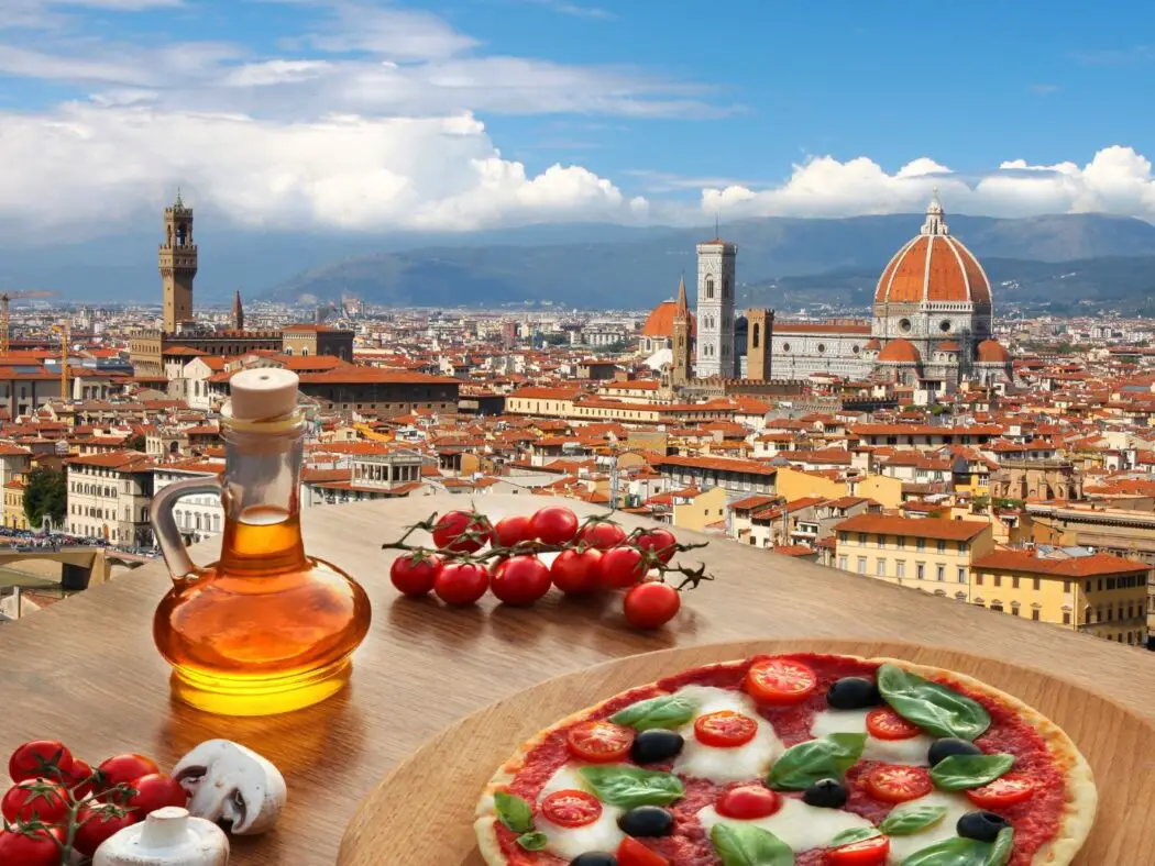 Close up view of olive oil, a plate of tomatoes and cheese, with rooftop views in the background