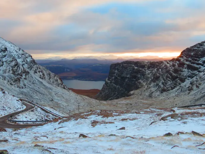 Snowy mountains with distant sunset and road in foreground