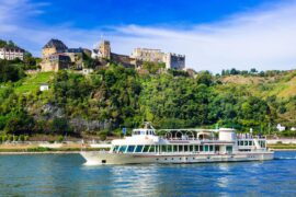 Boat cruising on a river surrounded by lush green riverbanks and a castle in the distance