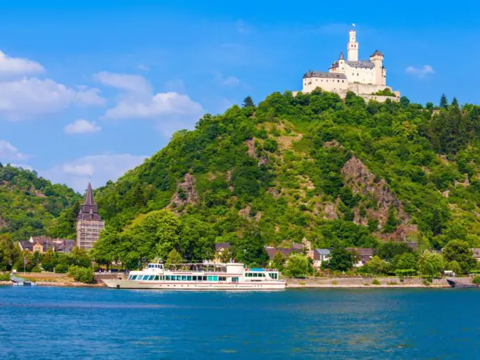 River with cruise boat on it, green forested hill in the background with a castle on top