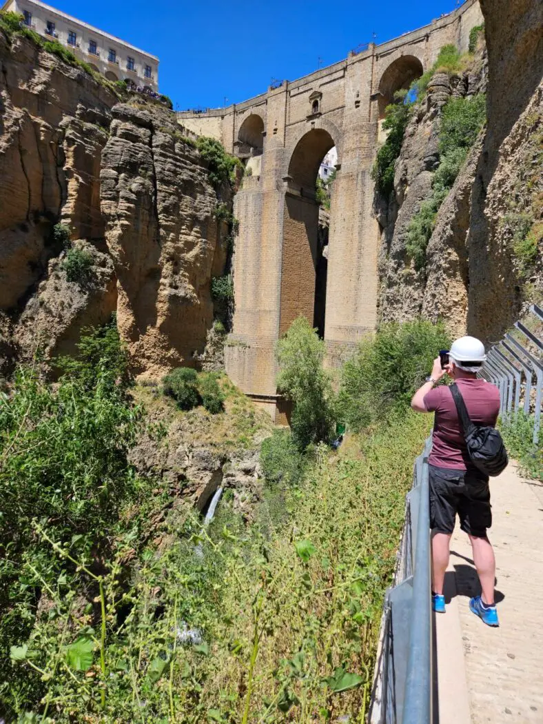 Man with white helmet taking a photo of a stone bridge