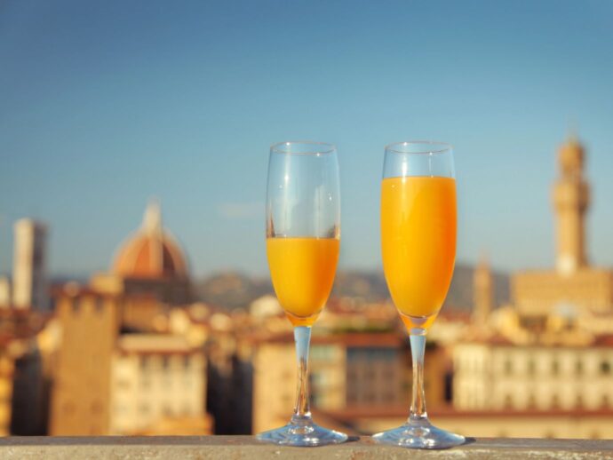 Two tall glasses of orange liquid against a city rooftop backdrop