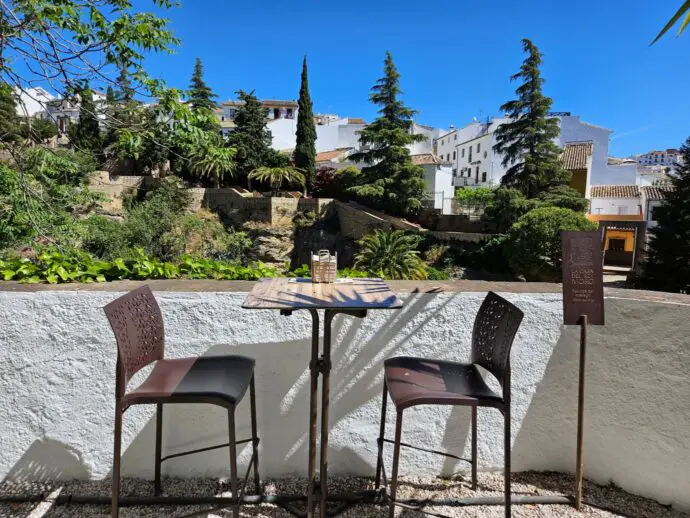 Two tall chairs beside a white wall overlooking a gorge with trees and houses