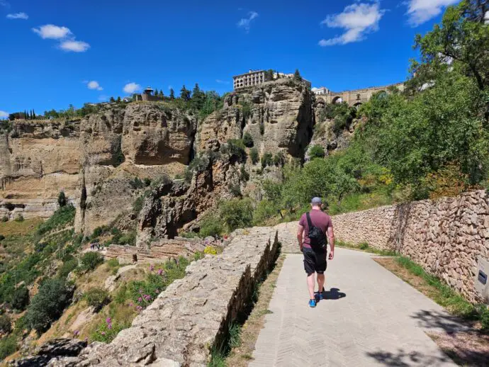 Path with man in purple t-shirt walking away towards a rocky cliff