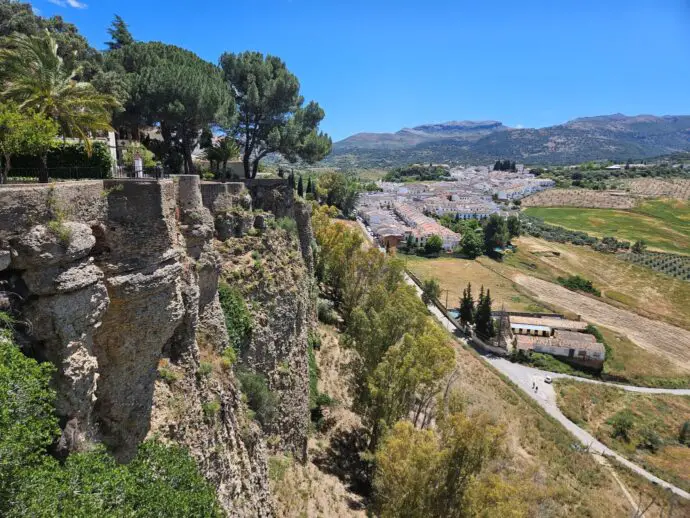 Rocky cliffs on the left with trees on top, and rural fields down below