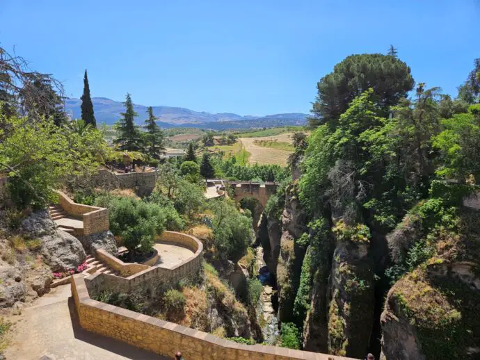 Lush green gorge with paved footpath running alongside with an old stone bridge in the distance