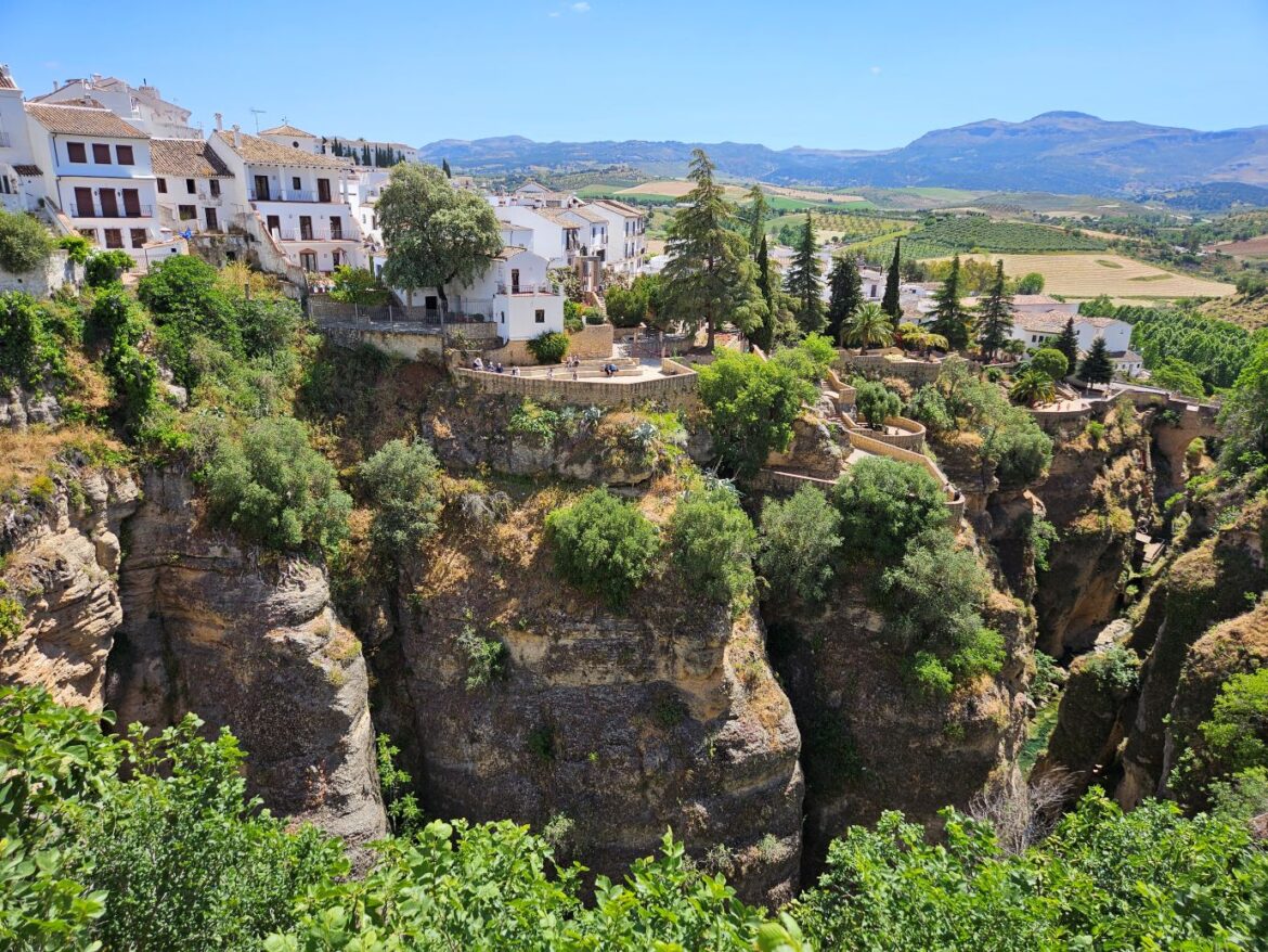 Steep-sided rocky gorge covered in green foliage with white buildings on top