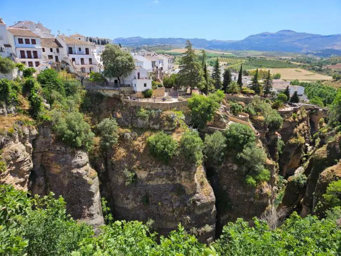 Steep-sided rocky gorge covered in green foliage with white buildings on top