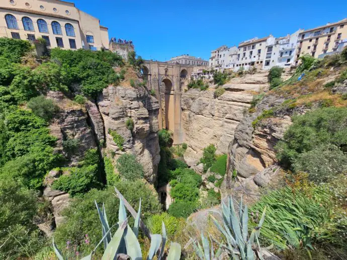 Lush green gorge with steep rocky cliffs and a stone bridge across the cliffs