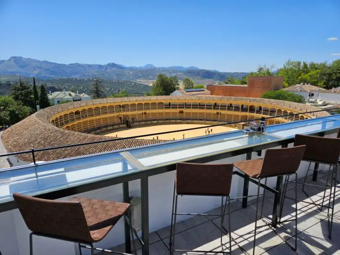 Tall stools on a terrace overlooking a bullring with mountains in the distance