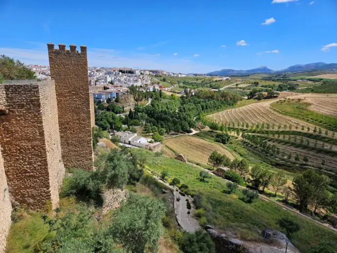 Old city wall on the left with green countryside below and a city in the background